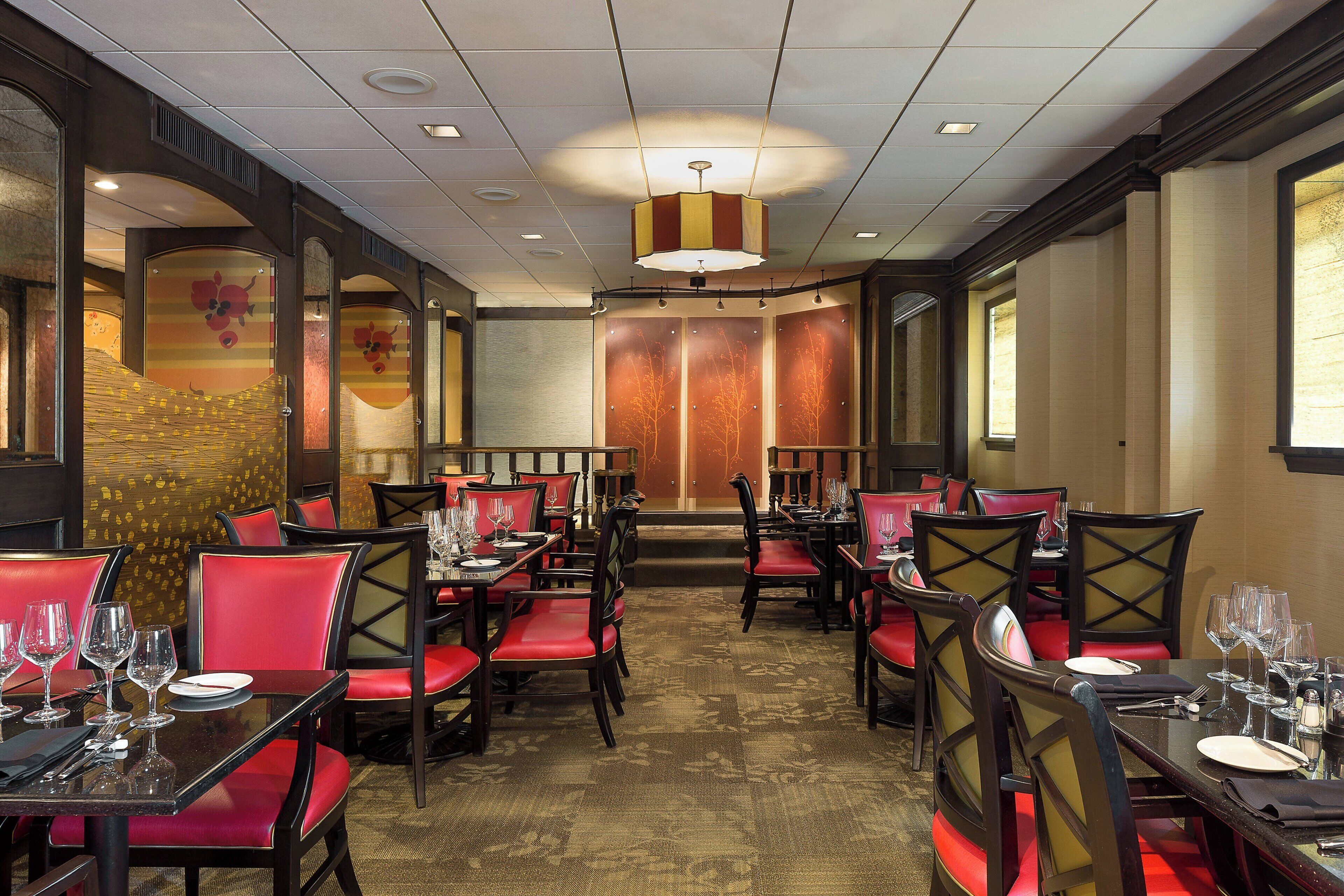 Un restaurant avec des chaises à revêtement rouge, des tables noires et un tapis à motifs.