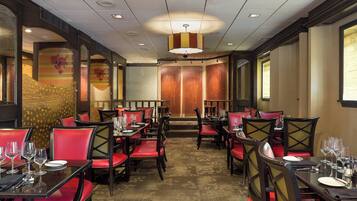 Un restaurant avec des chaises à revêtement rouge, des tables noires et un tapis à motifs.