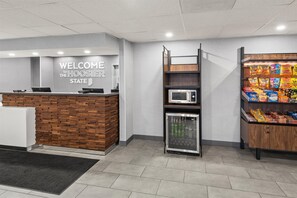 A reception area with a wooden reception desk, a welcome sign, a microwave, a refrigerator, and snack dispensers. - Hampton Inn Indianapolis-N.E./Castleton (Indianapolis)