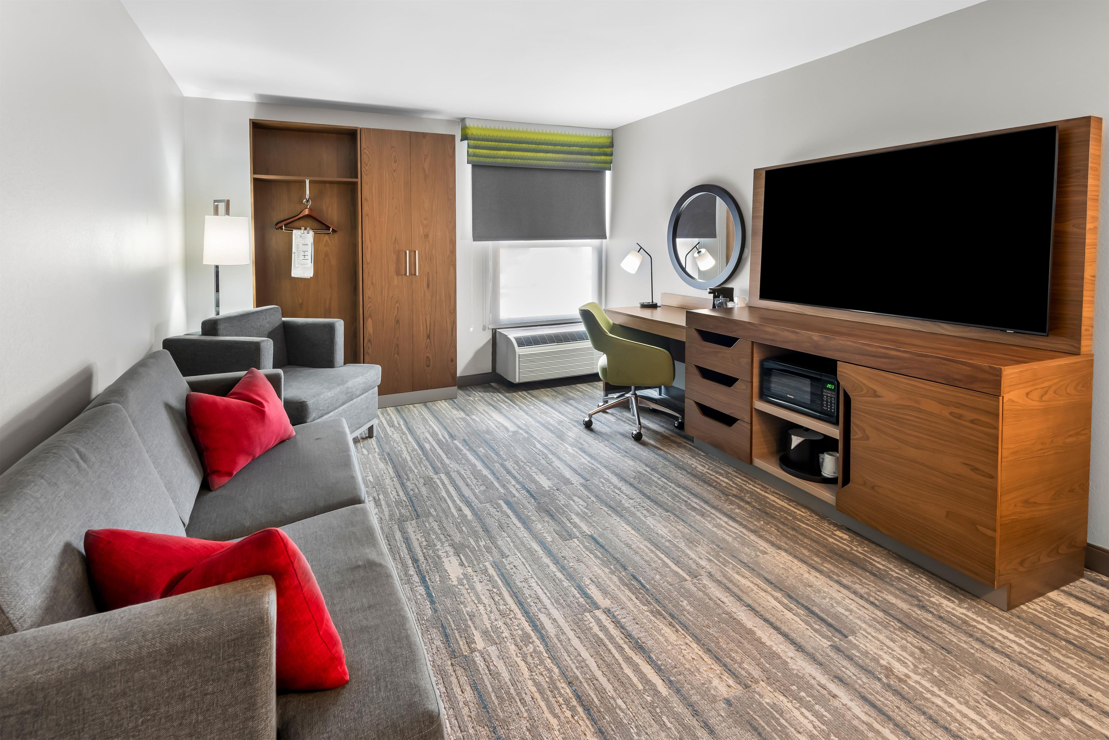 A hotel room with a sofa, desk, television, and wardrobe.