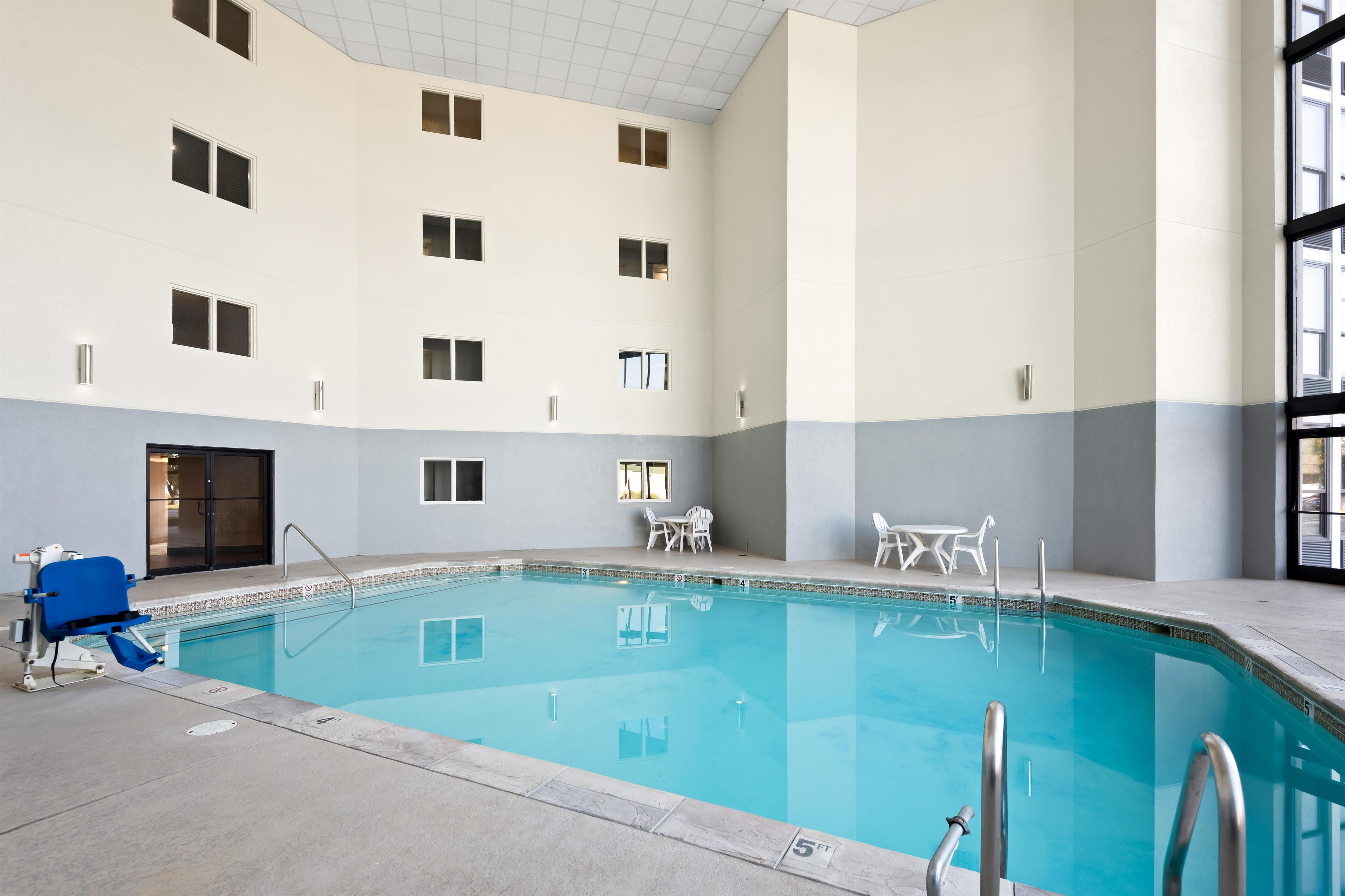 Una piscina interior con vistas despejadas del área de la piscina, incluyendo el borde de la piscina, una silla de salvavidas y un conjunto de escaleras que bajan a la piscina.