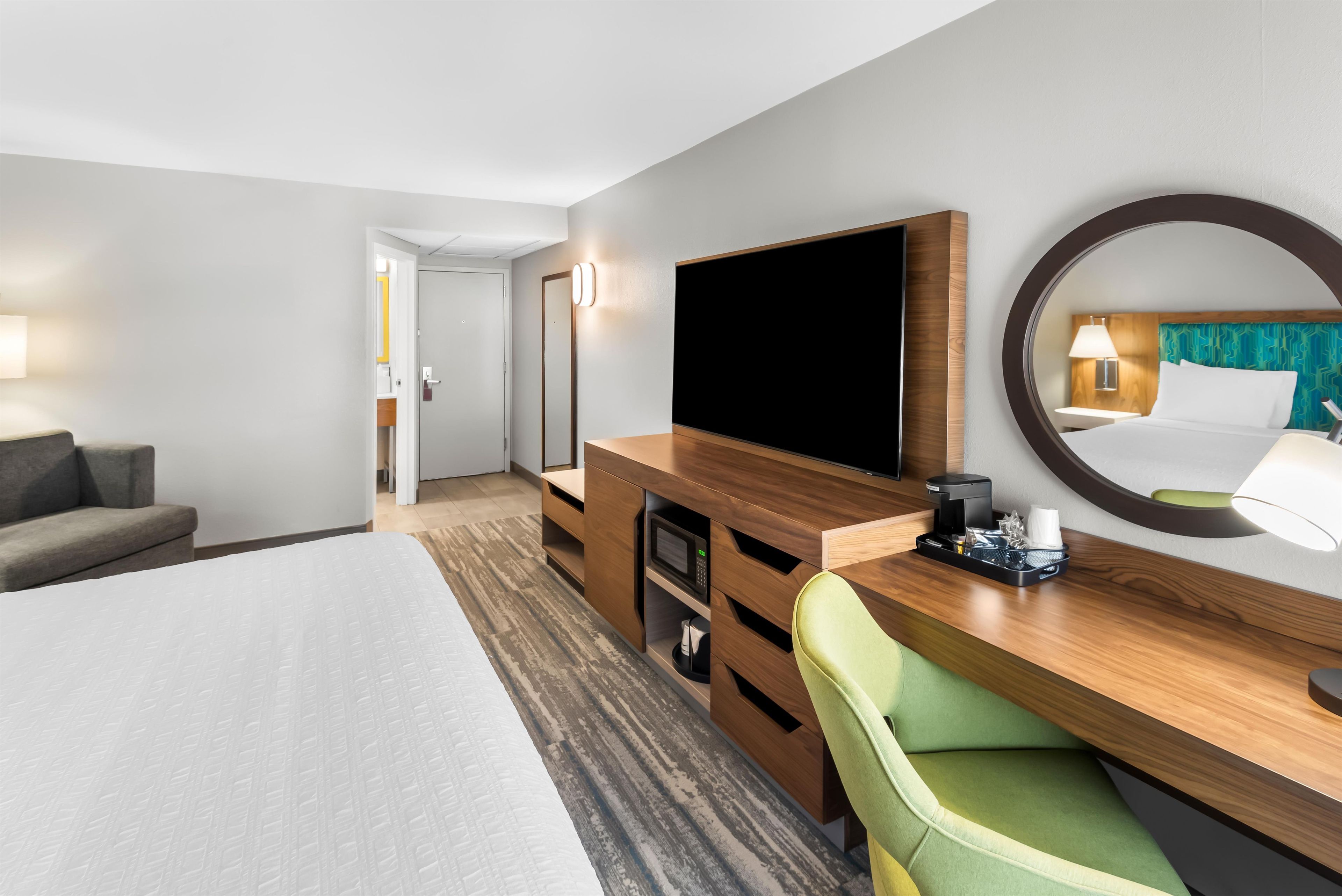 Une chambre d’hôtel comprenant un lit, une télévision, un bureau avec une chaise, un miroir et une porte donnant sur une salle de bain.