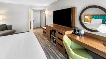 Une chambre d’hôtel comprenant un lit, une télévision, un bureau avec une chaise, un miroir et une porte donnant sur une salle de bain.
