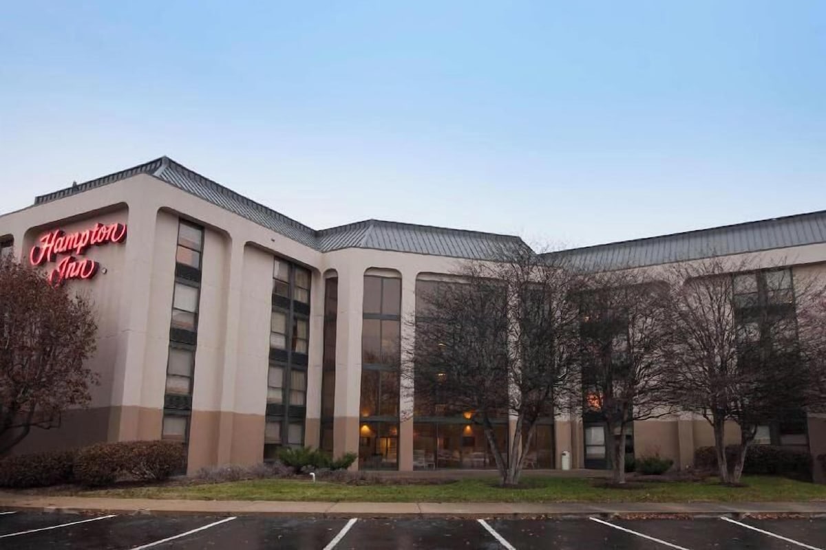 A Hampton Inn building with a large sign, multiple windows, and a parking lot.