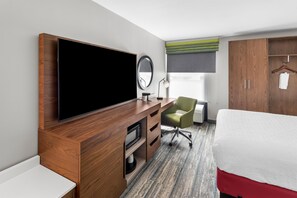 A hotel room with a large flat-screen TV, a desk with a chair, a bed, a wardrobe, and a window with a view.