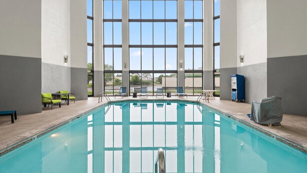 An indoor swimming pool with clear glass walls, a tiled floor, and several lounge chairs.