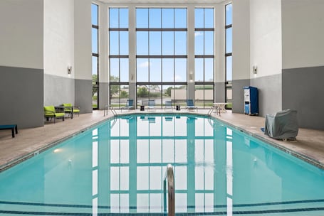An indoor swimming pool with clear glass walls, a tiled floor, and several lounge chairs.