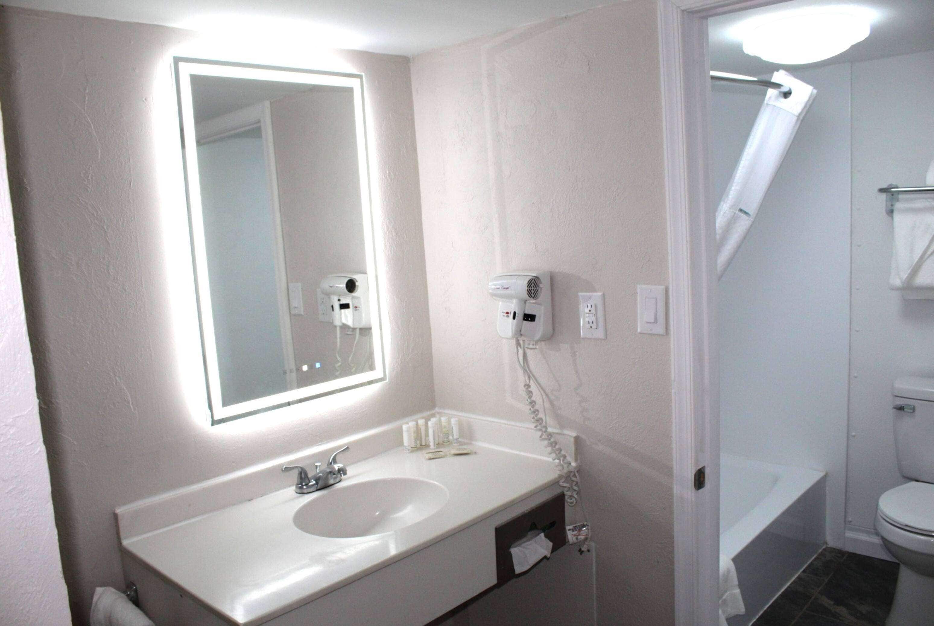 Un baño con lavamanos blanco, espejo y un secador de pelo en la pared.
