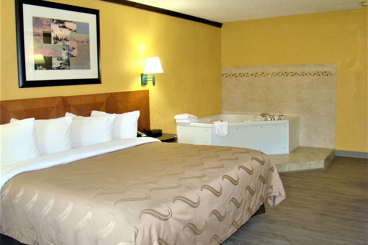 A hotel room with a large bed, a white bathtub, and a wall-mounted lamp.