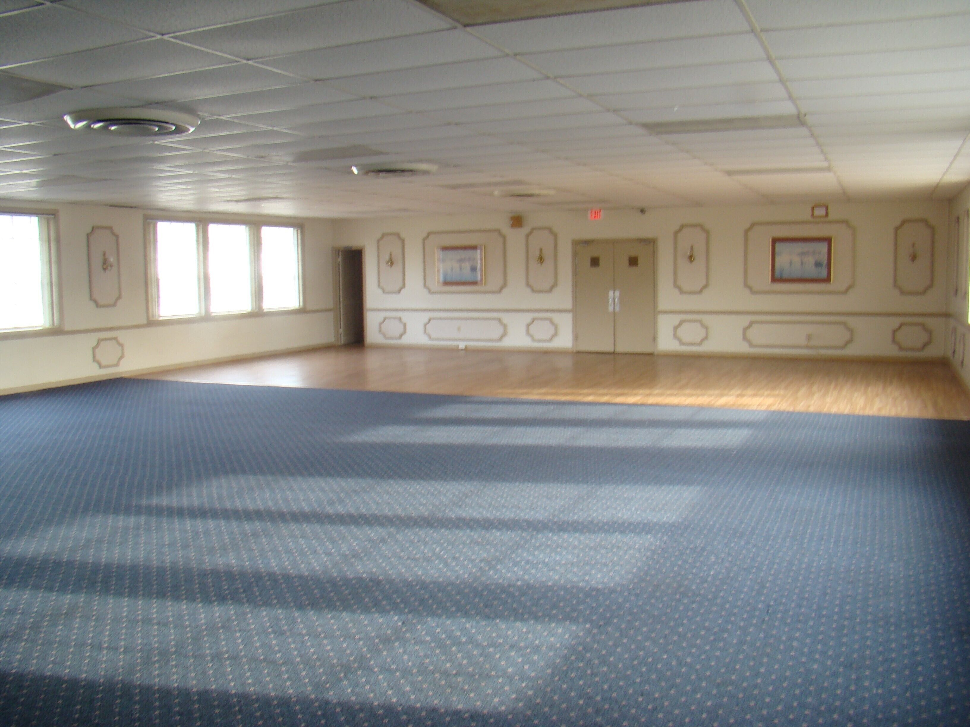 A large, empty room with a patterned carpet, wooden flooring, and a door with a small picture frame.