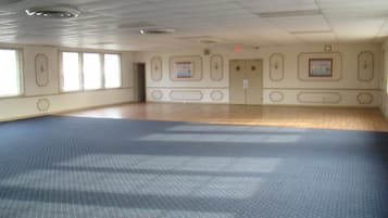 A large, empty room with a patterned carpet, wooden flooring, and a door with a small picture frame.