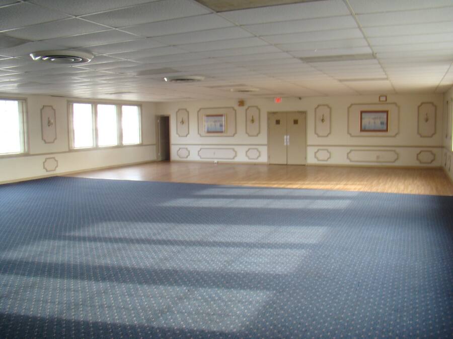 A large, empty room with a patterned carpet, wooden flooring, and a door with a small picture frame.