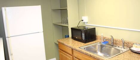 A compact kitchen with a white refrigerator, a microwave, a sink, and wooden cabinets.
