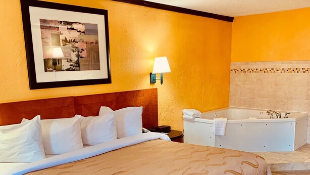 A hotel room with a large bed, a bathroom with a bathtub, and a framed picture on the wall. - Baymont by Wyndham Front Royal Near Shenandoah National Park (Front Royal)