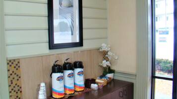 A kitchen counter with three coffee makers, a framed picture above, and a vase of white flowers.