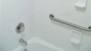 A white bathroom with a shower, grab bar, and a small soap dish.