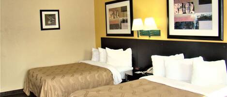 A hotel room with two beds, a nightstand, a lamp, and framed pictures on the wall.