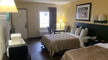 Habitación de hotel con dos camas, un escritorio, una silla, una lámpara, un calefactor y un cuadro en la pared.