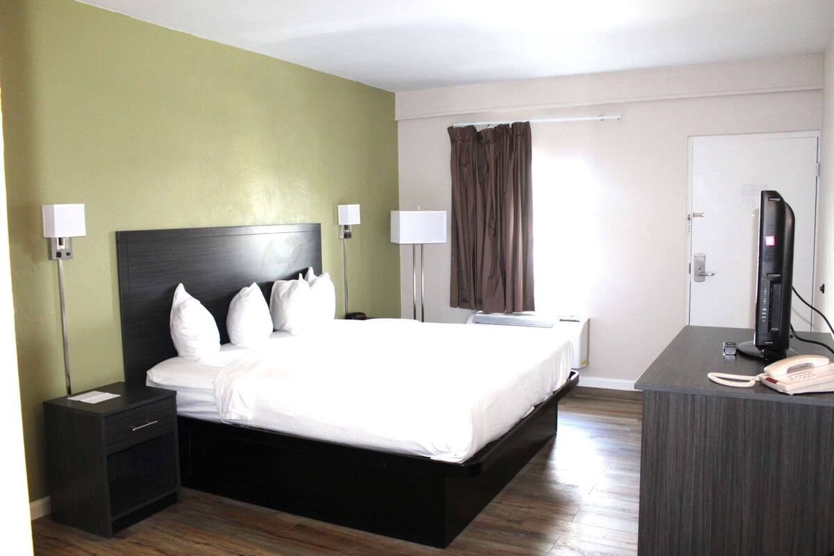 A hotel room with a large bed, two bedside tables with lamps, a desk with a telephone, and a television.