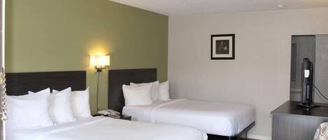 Habitación de hotel con dos camas individuales, un escritorio, una silla, una lámpara y un cuadro en la pared.