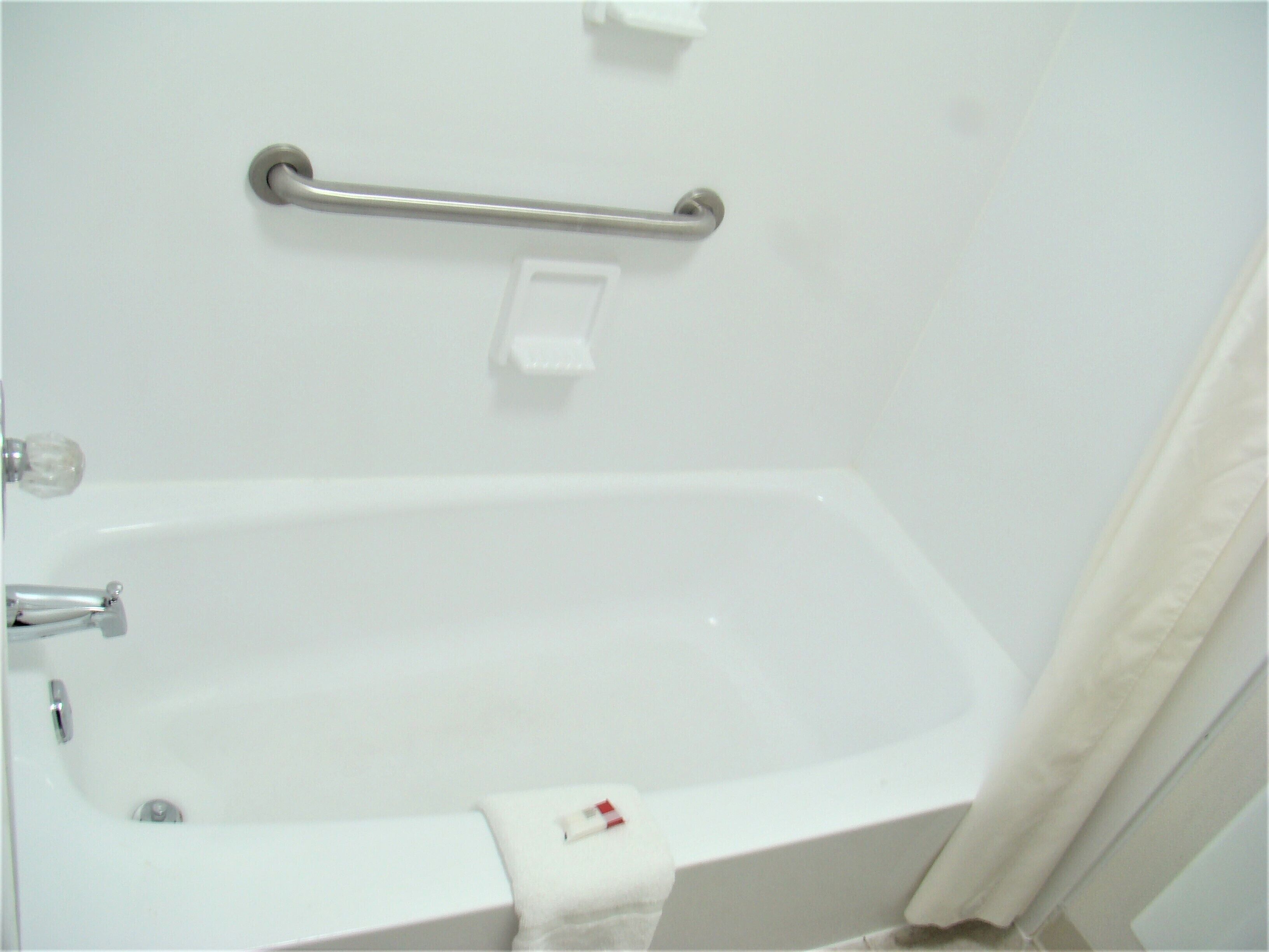 A white bathtub with a grab bar and a white towel.