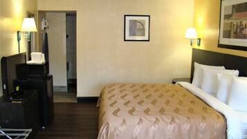 A hotel room with a bed, bedside lamps, a desk with a lamp, a framed picture on the wall, and a door leading to another room.