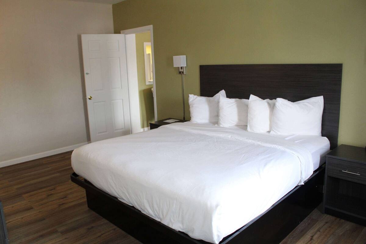 A neatly made bed with white linens in a hotel room with a wooden floor and a green wall.