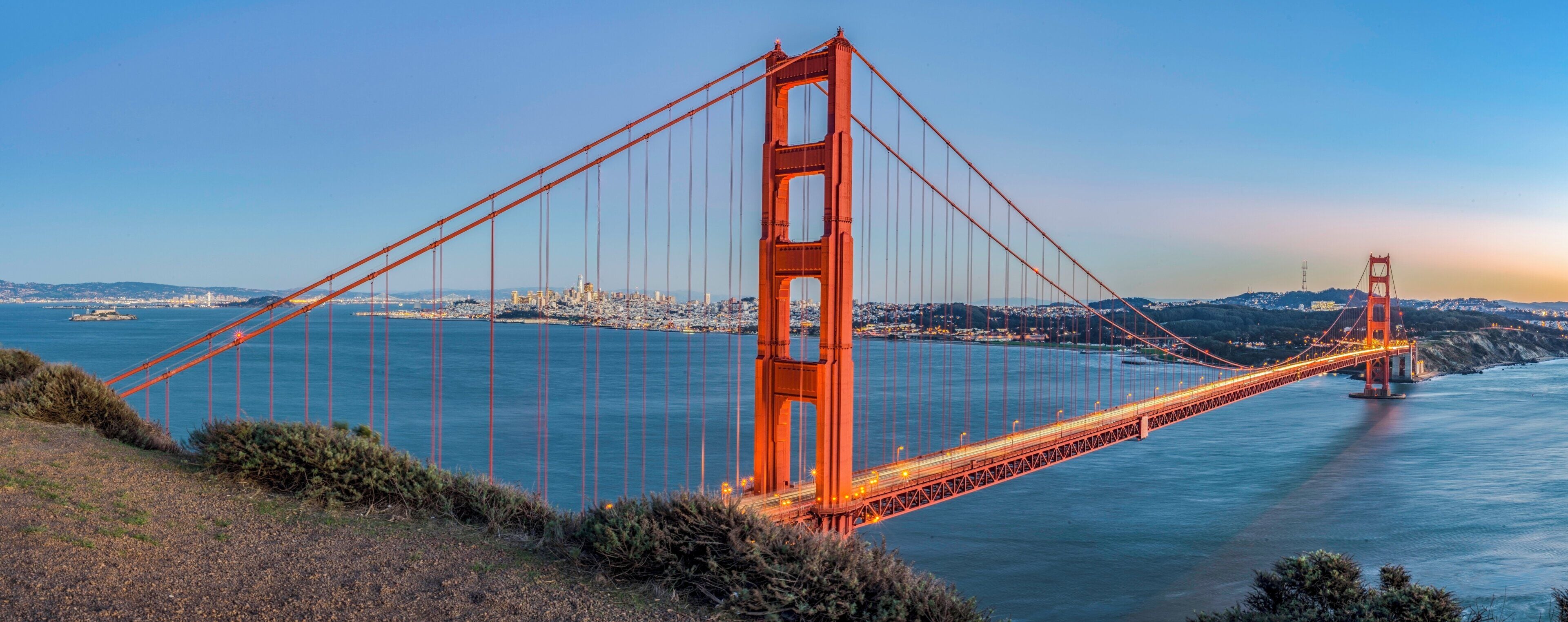 A large suspension bridge spanning a body of water with a cityscape in the background.