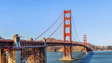 A large suspension bridge with a prominent tower and cables, spanning a body of water with hills in the background.
