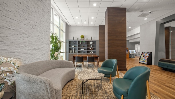 Una moderna hall con un divano grigio, poltrone color acquamarina, un pavimento in legno, una libreria e un'area reception.