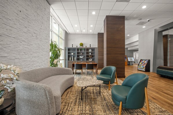 A modern lobby with a grey sofa, teal chairs, a wooden floor, a bookshelf, and a reception area. - Holiday Inn Golden Gateway by IHG (San Francisco)