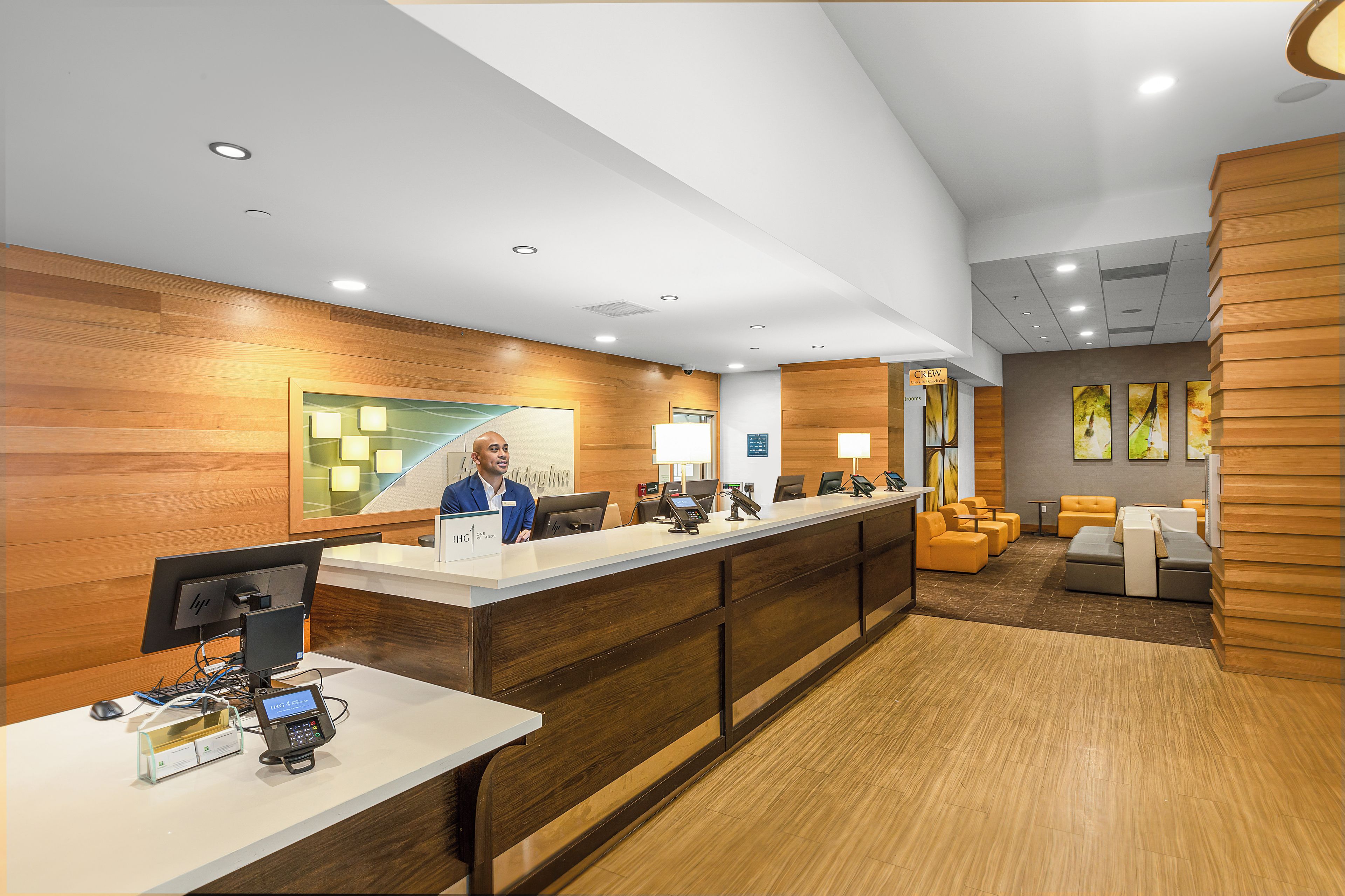 A hotel reception area with a wooden reception desk, computers, and seating area with sofas.