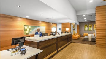 A hotel reception area with a wooden reception desk, computers, and seating area with sofas.