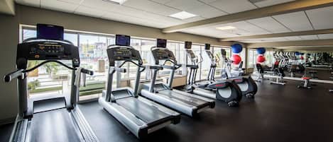 A gym with multiple treadmills, exercise balls, and a view of the city through large windows.