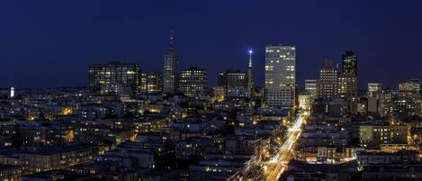 A nighttime cityscape with a dense cluster of buildings, including high-rise structures and a variety of architectural styles.
