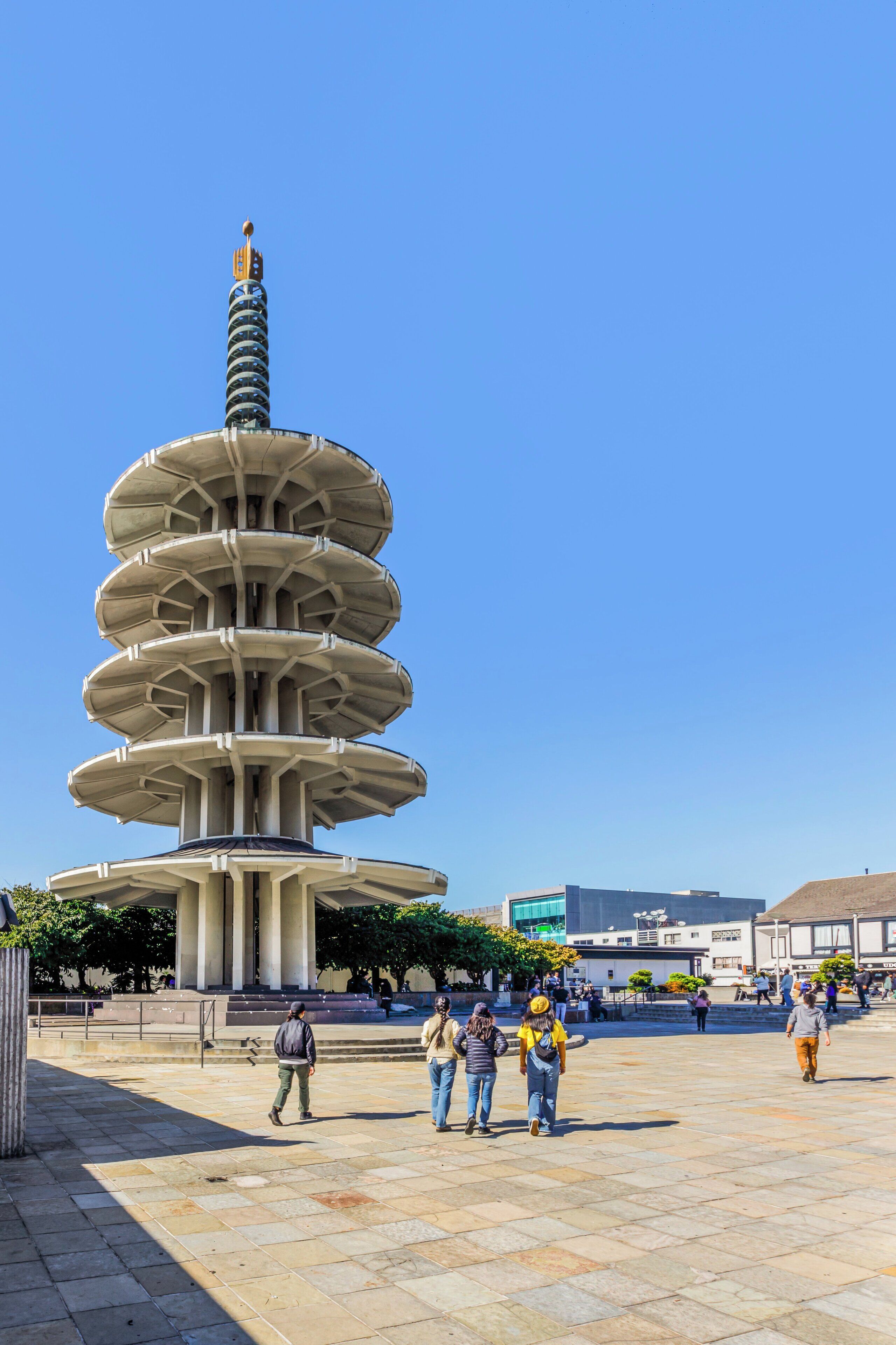 A multi-tiered tower structure with a spiral staircase, surrounded by a plaza with people walking.