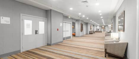 A hotel corridor with doors, a patterned carpet, and a seating area with a lamp.