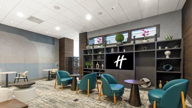 En modern hotellobby med turkosa fåtöljer, en stor TV-skärm och en dekorativ vägg med hyllor.