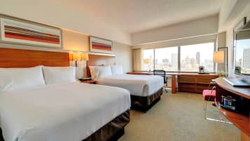A hotel room with two beds, a desk, a chair, and a large window offering a city view.