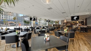 En rymlig restaurang med många bord och stolar, stora fönster och en modern inredning.