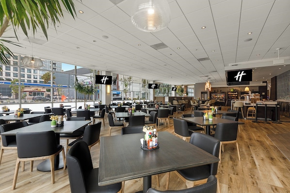 Um restaurante espaçoso com várias mesas e cadeiras, grandes janelas e design de interiores moderno.