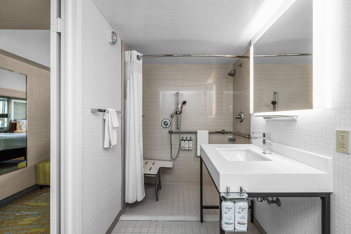 A modern bathroom with a double sink, a shower with a handheld showerhead, a towel rack, and a mirror.