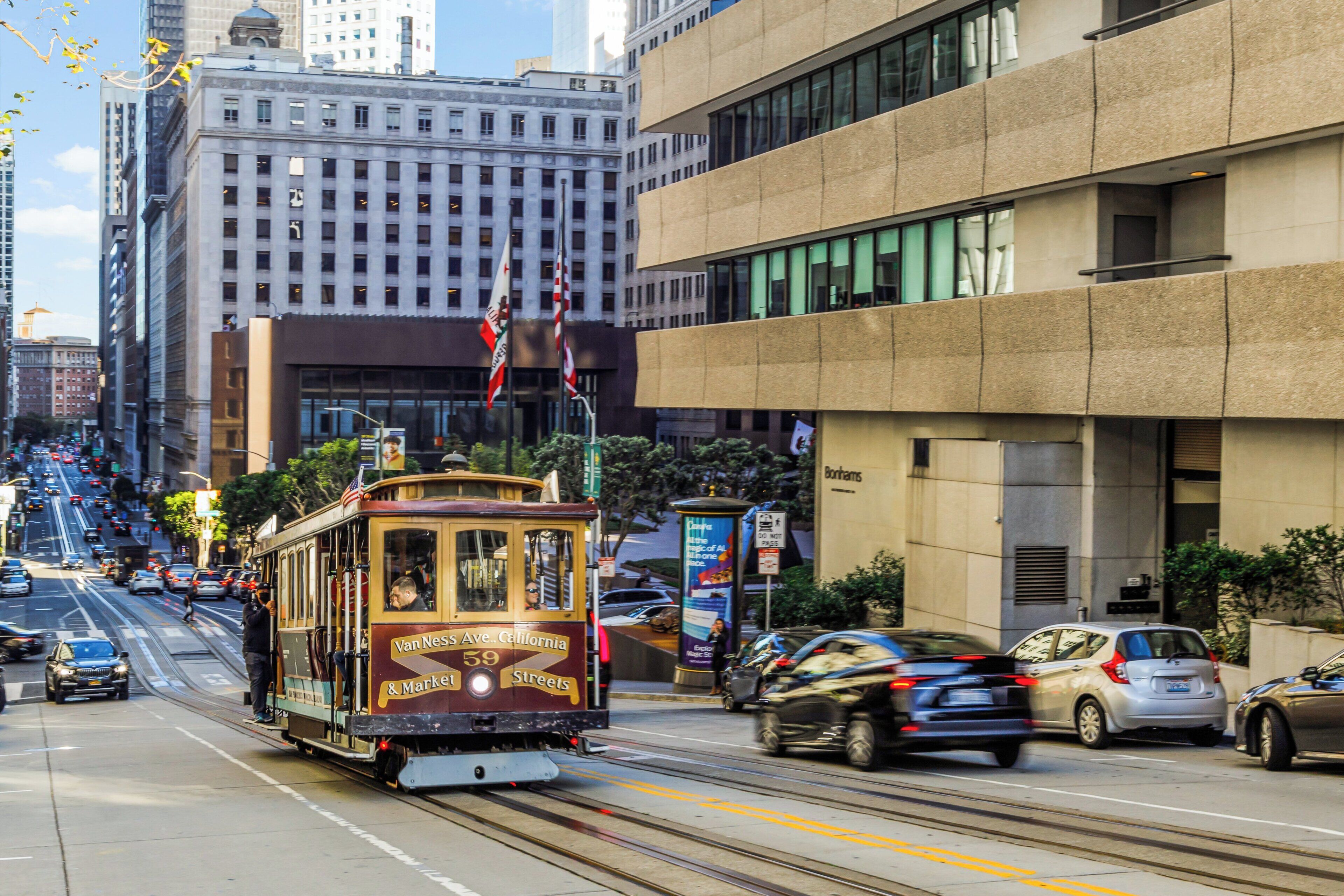 A cable car on a street with buildings and cars.
