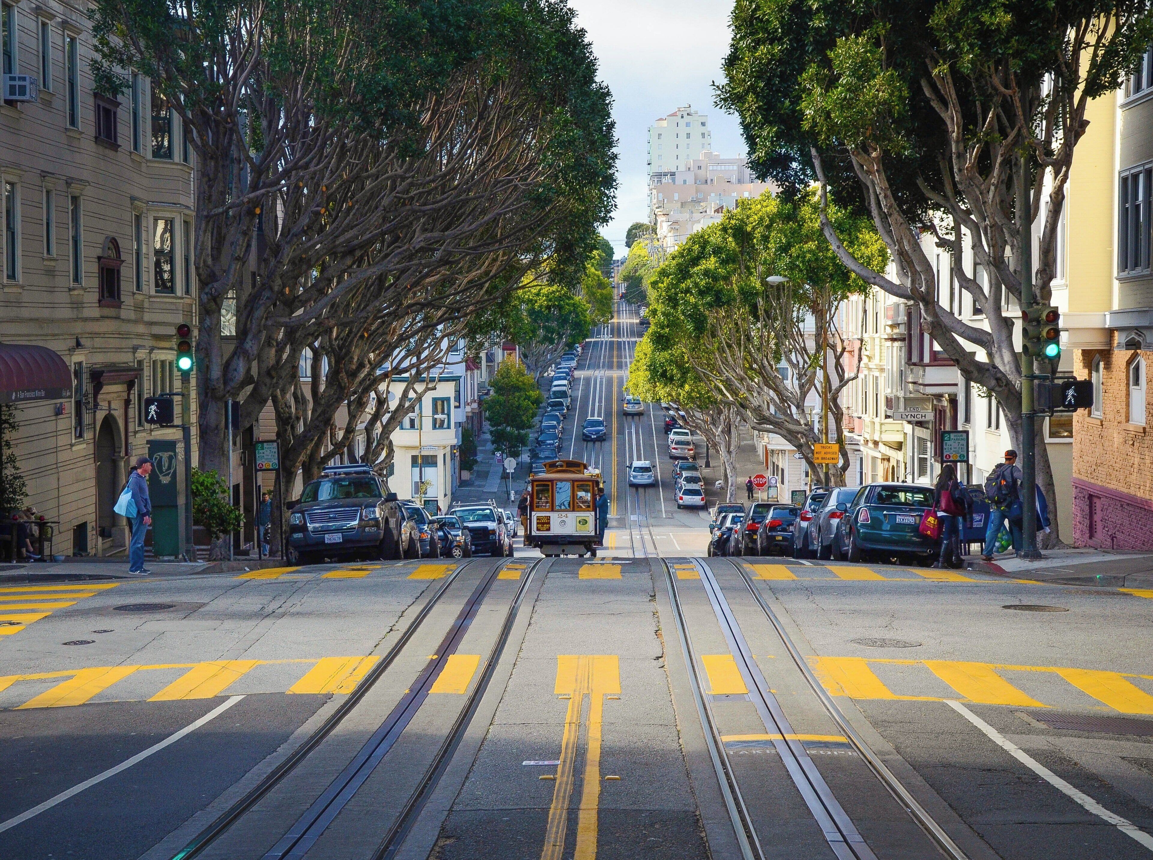 A street with tram tracks, parked cars, and buildings.