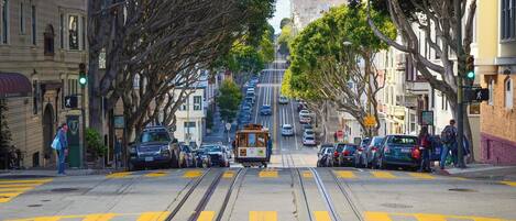 A street with tram tracks, parked cars, and buildings.
