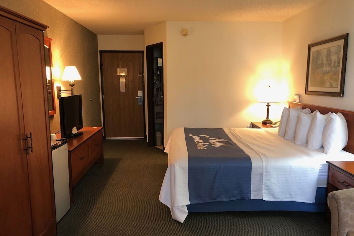 A hotel room with a bed, a desk with a lamp, a television, a wardrobe, and a door leading to another room.