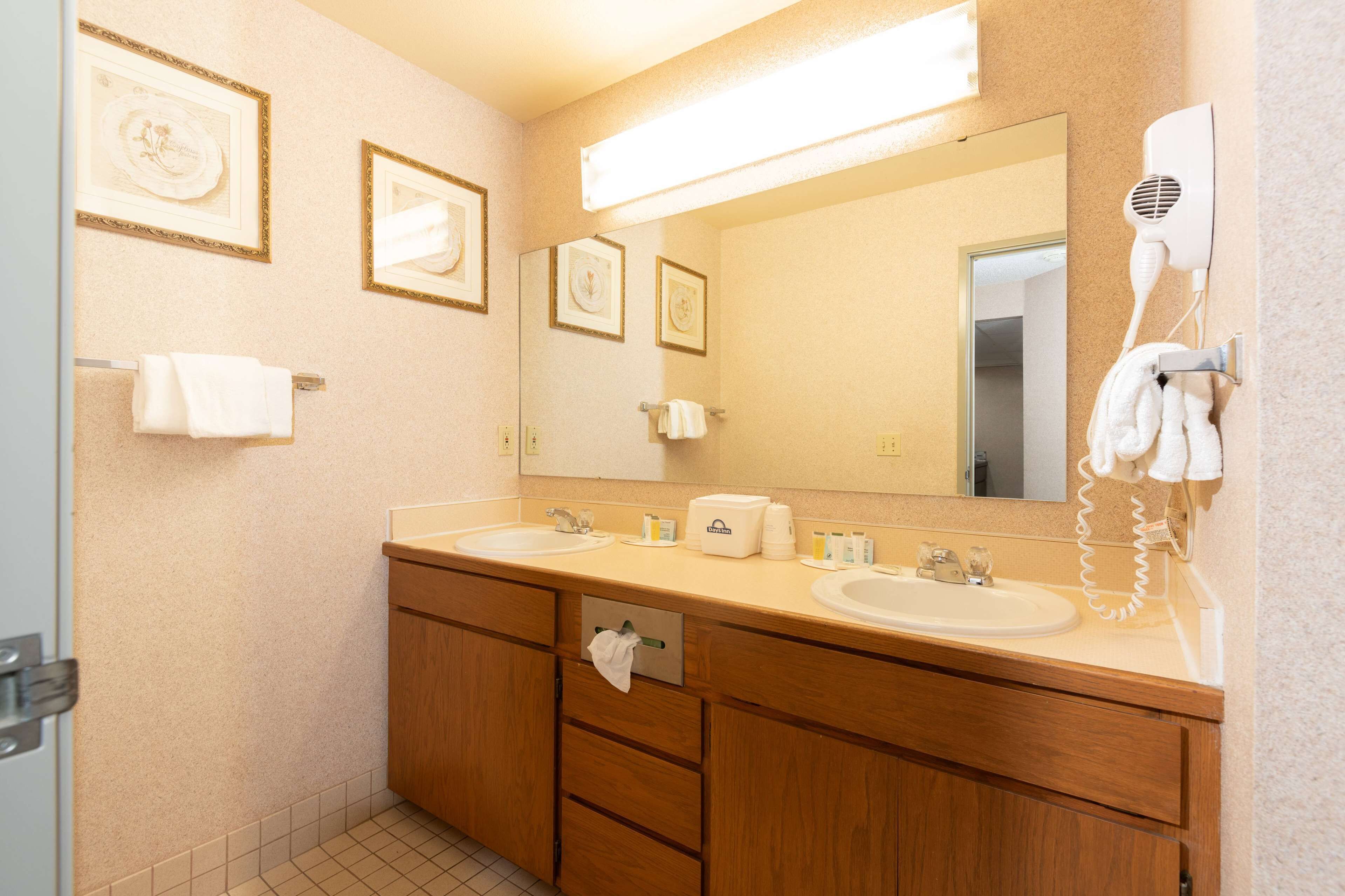 Une salle de bain d’hôtel avec deux lavabos, un miroir, des tableaux encadrés au mur et un sèche-cheveux fixé au mur.