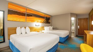 Et hotelværelse med to senge, et skrivebord og et stort maleri af en solnedgang.