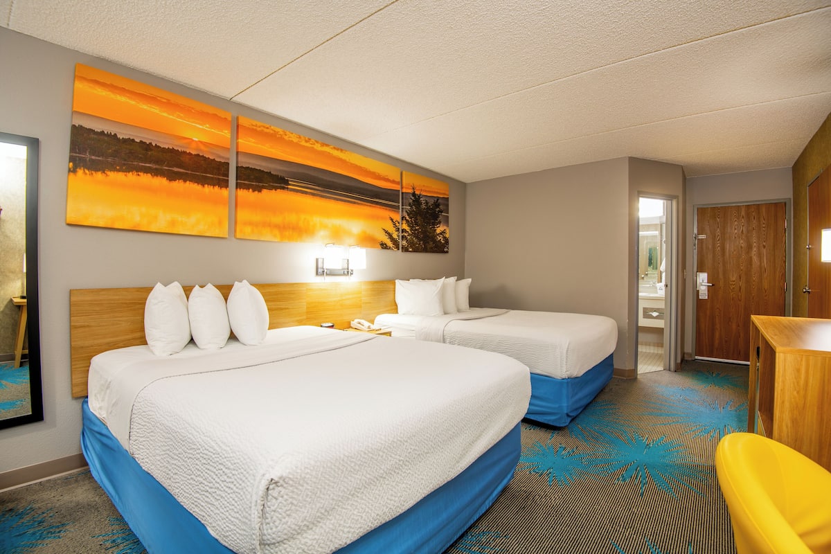 A hotel room with two beds, a desk, and a large painting of a sunset.