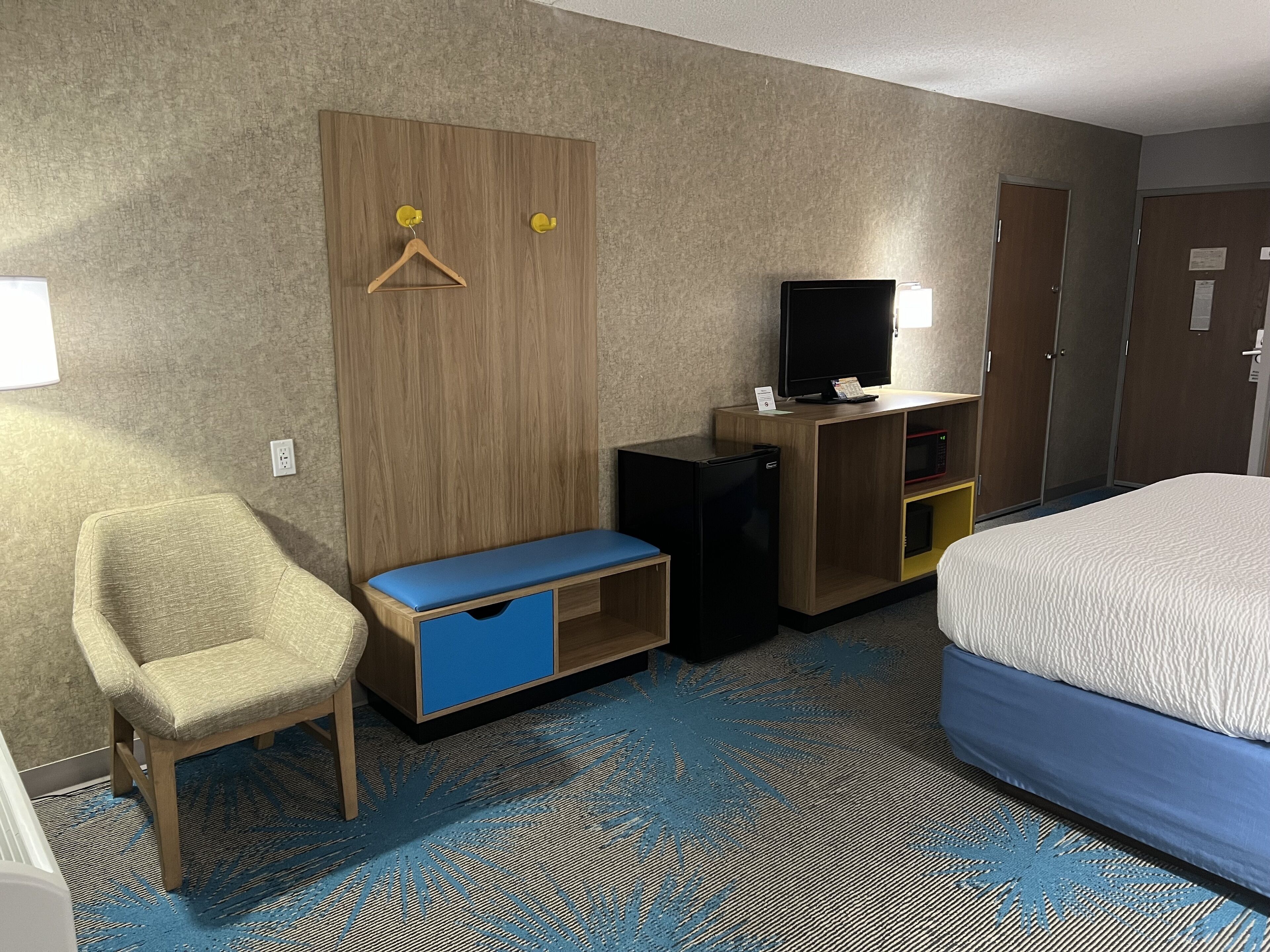A hotel room with a bed, a desk with a TV, a chair, and a wardrobe.
